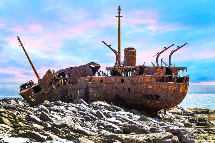 Explore iconic island landmarks – Plan your day trip or book return ferry tickets to the Aran Islands for 2026 The rusted, historic hull of the MV Plassey shipwreck resting on the rugged limestone shoreline of Inisheer island under a striking blue sky